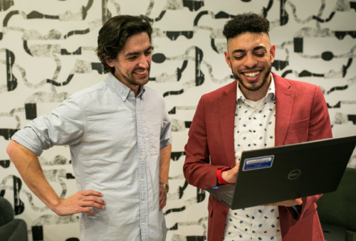 Two men standing in front of a laptop.